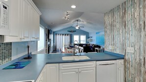Een moderne keuken met witte kastjes, een blauw aanrecht en een eethoek met een tafel en stoelen.