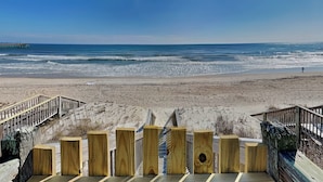 Een houten looppad dat naar een strand leidt, met een pier op de achtergrond.