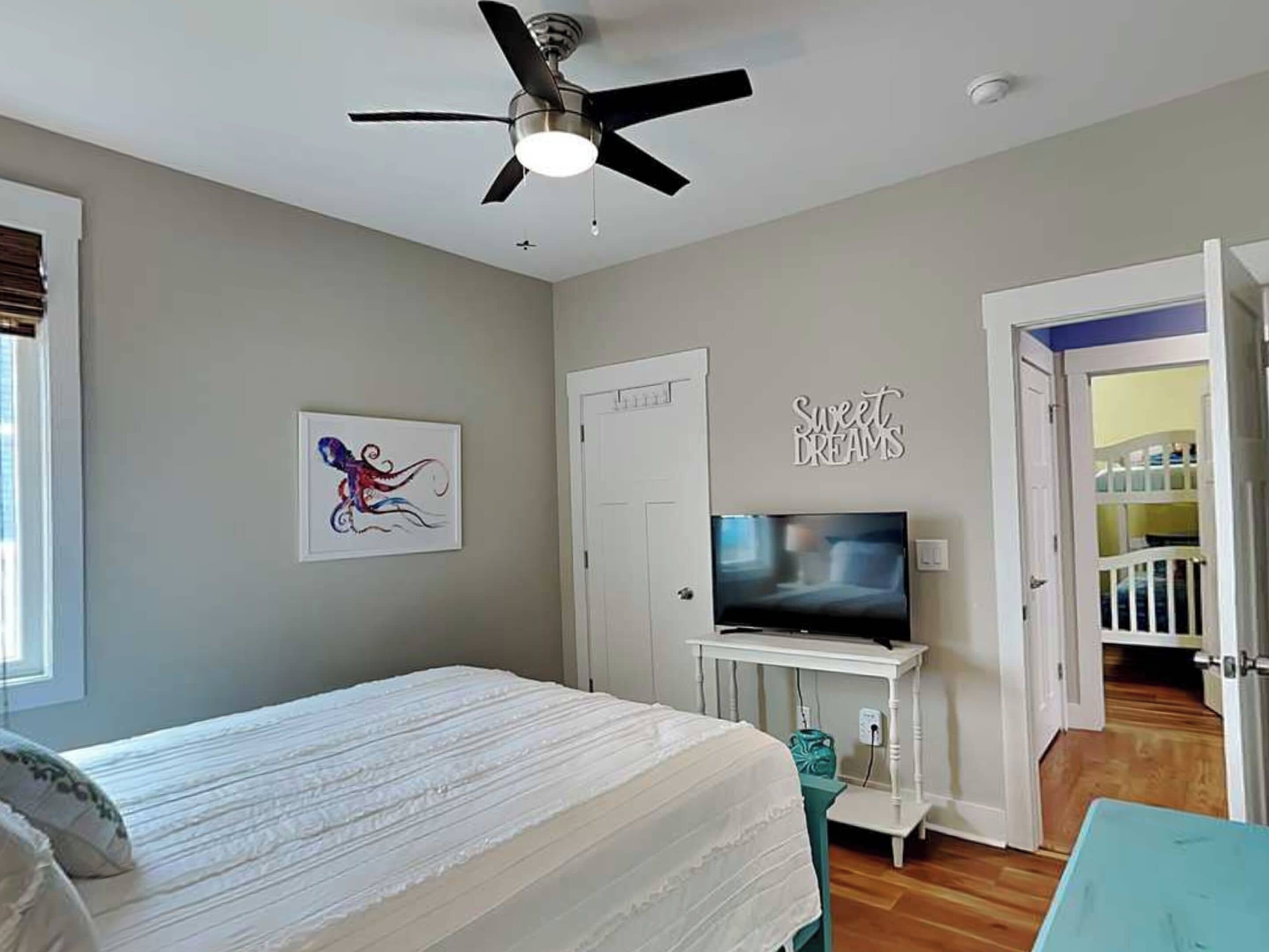 A bedroom with a bed, a ceiling fan, a television, and a wall with a 'Sweet Dreams' sign.