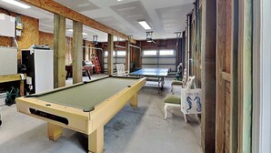 Una mesa de billar en una habitación con vigas de madera, una silla blanca y una mesa con diseño de caballito de mar.