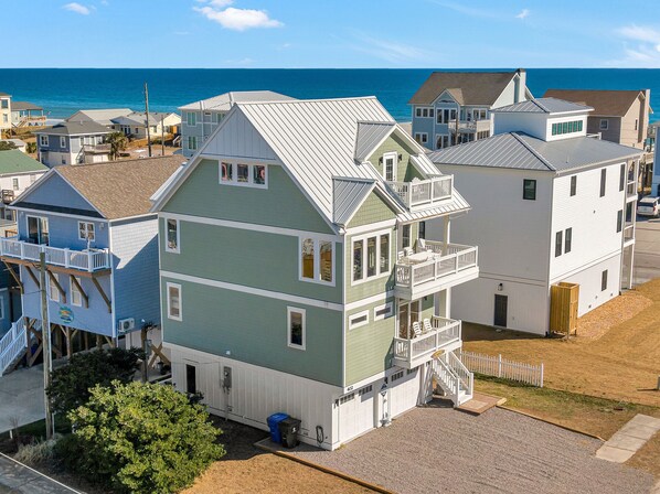 A multi-story building with a balcony on the second floor, a covered porch on the ground floor, and a view of the ocean. - Shore Sounds Fun by Topsail Realty (Holly Ridge)
