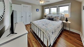 Un dormitorio con cama, mesitas de noche, ventilador de techo, ventana y puerta.