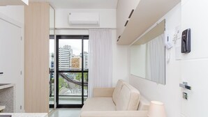 A modern hotel room with a balcony, a sofa, a lamp, and a view of the cityscape. - Start - Gonzaga Stays (Curitiba)