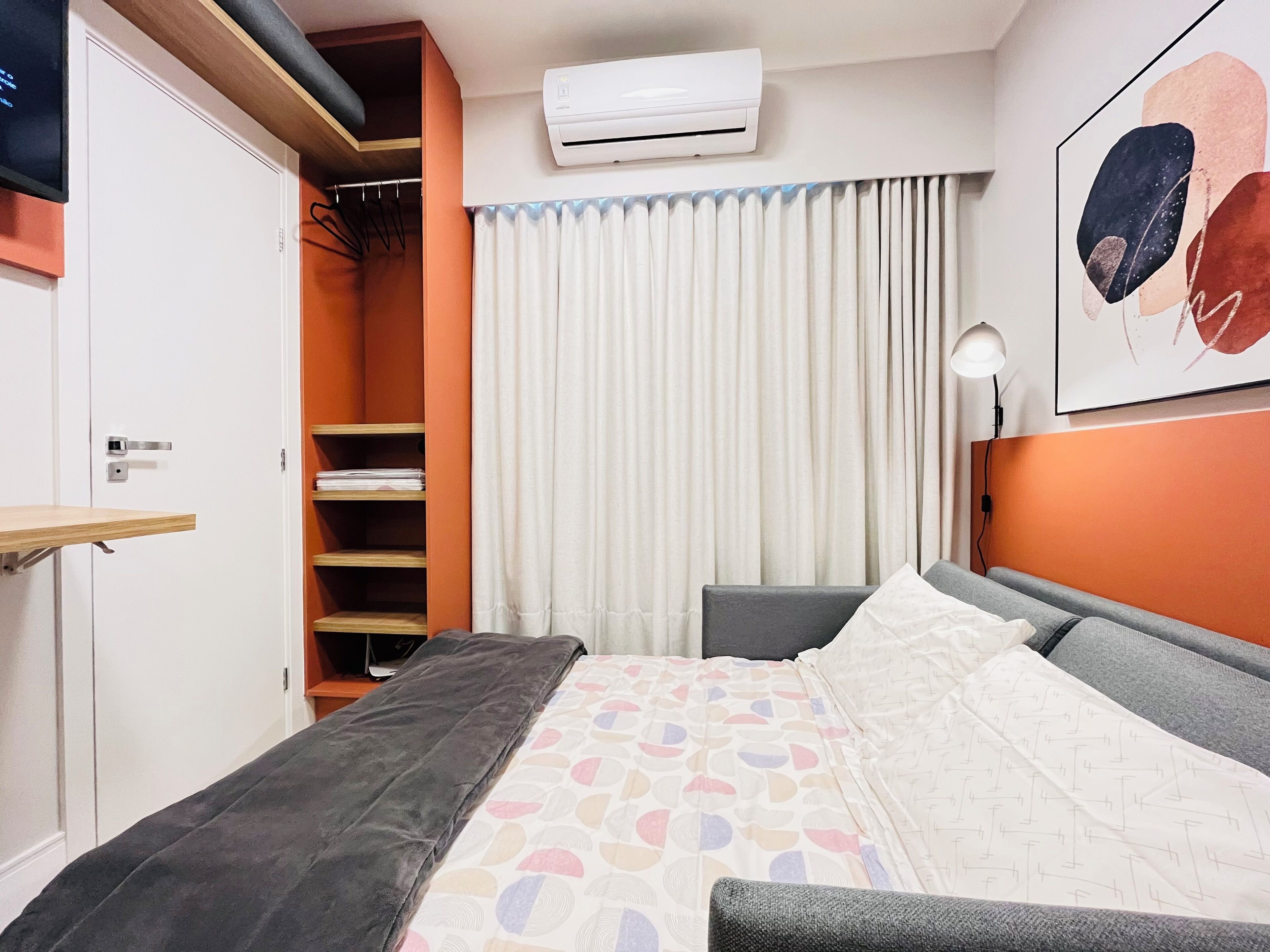A bedroom with a bed, a wardrobe, a desk, and a wall-mounted air conditioner.