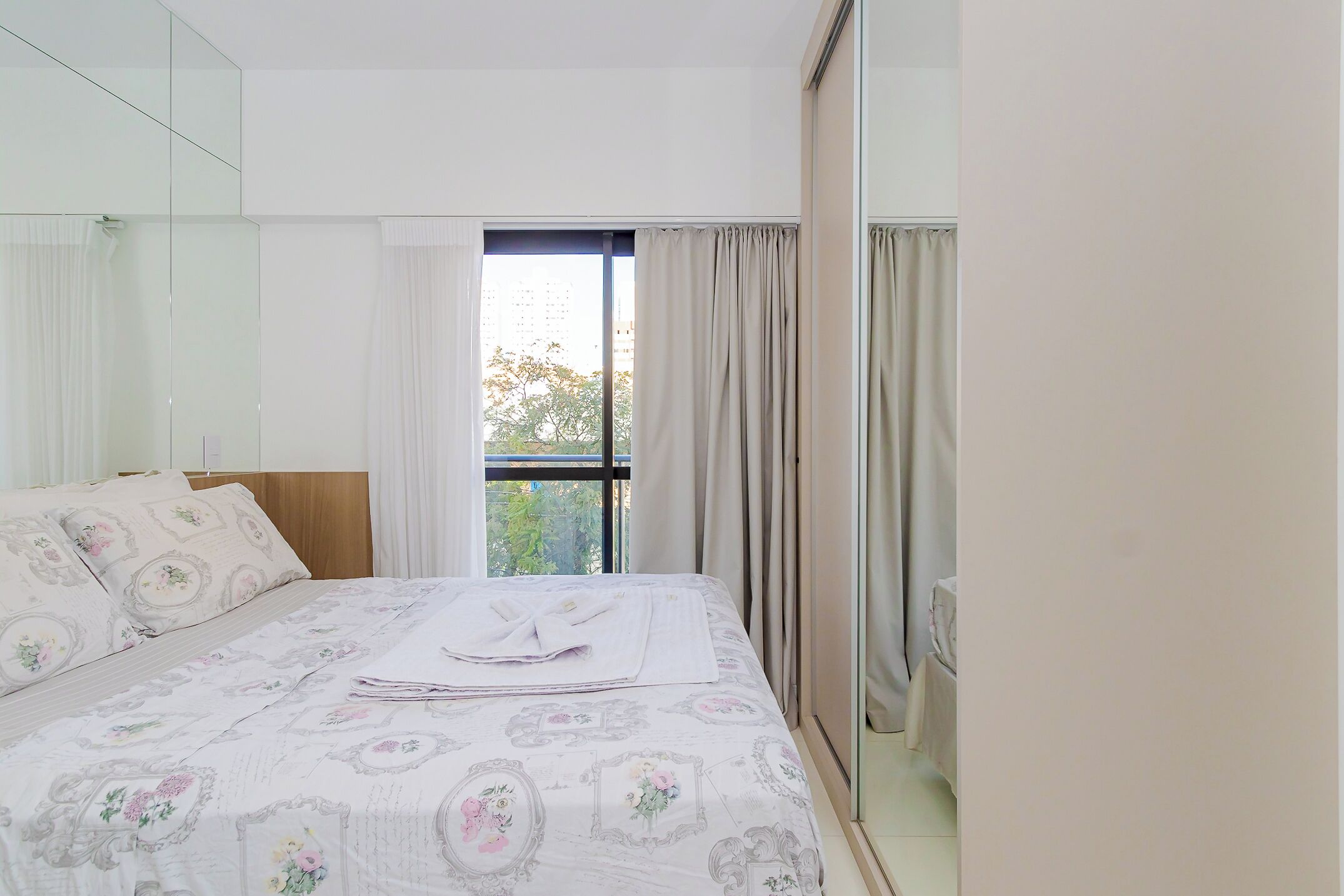 A bedroom with a large bed, a window with curtains, and a view of trees outside.