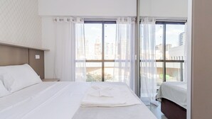 A hotel room with a large bed, a nightstand, and a window with curtains. - Start - Gonzaga Stays (Curitiba)