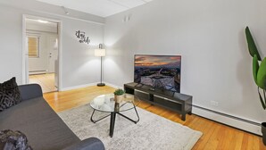 A modern living room with a gray sofa, a glass coffee table, a painting of a sunset, a floor lamp, and a TV stand. - Salem 2B rep (Arlington Heights)