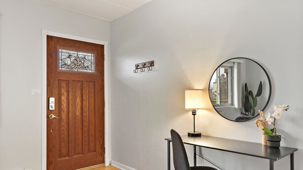 A room with a wooden door, a coat hook, a desk with a chair, a lamp, and a potted orchid. - Salem 2B rep (Arlington Heights)