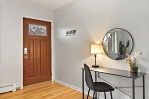 A room with a wooden door, a coat hook, a desk with a chair, a lamp, and a potted orchid. - Salem 2B rep (Arlington Heights)