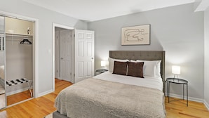 A bedroom with a large bed, a bedside table with a lamp, a mirror, a wardrobe, and a door leading to another room. - Salem 2B rep (Arlington Heights)