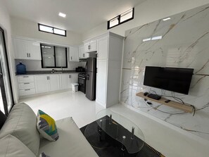 Una cocina moderna con armarios blancos, horno empotrado y refrigerador. Hay un televisor de pantalla plana montado en la pared y una cafetera en la encimera.