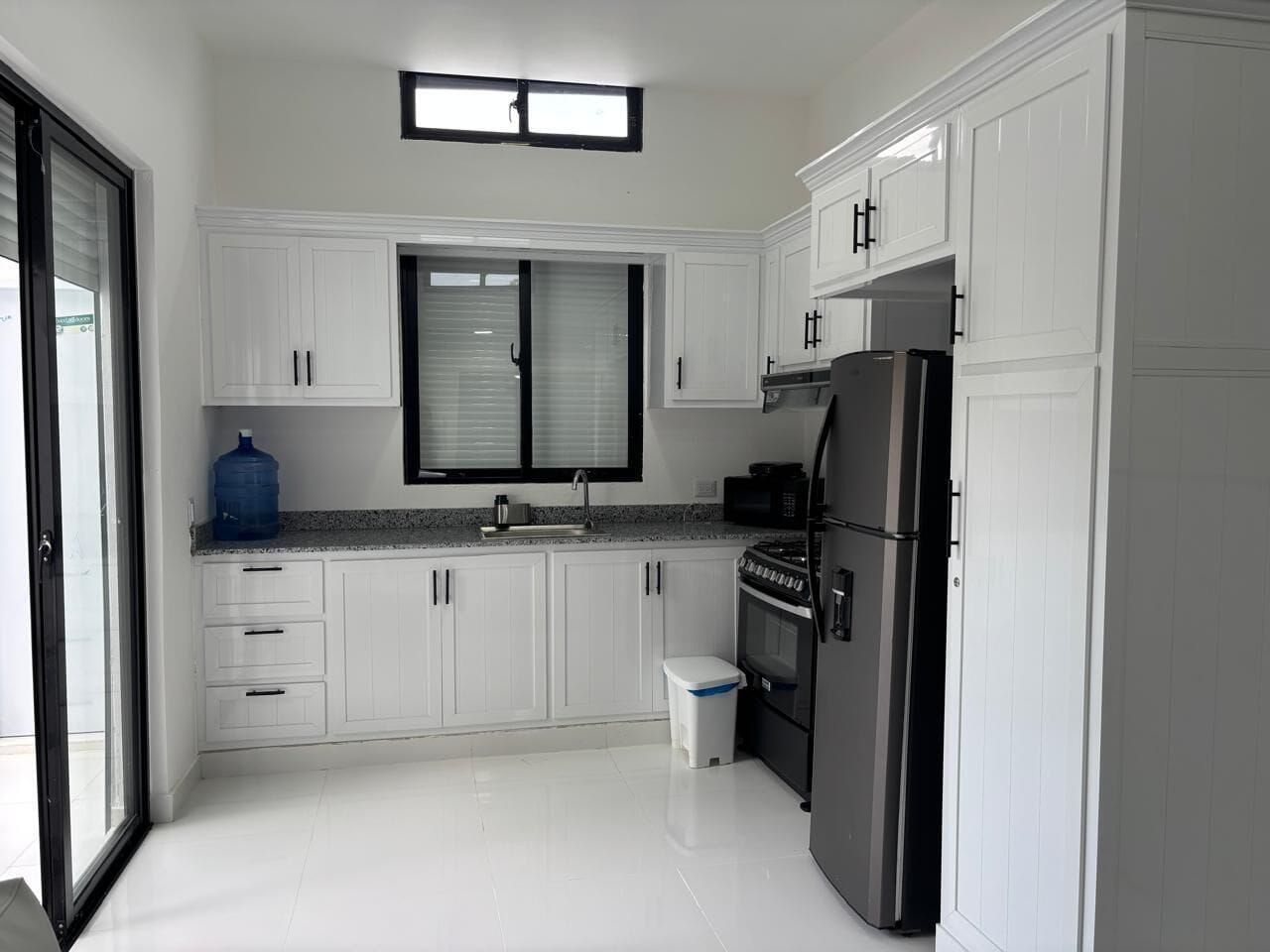 A modern kitchen with white cabinets, a stainless steel refrigerator, and a large water dispenser.