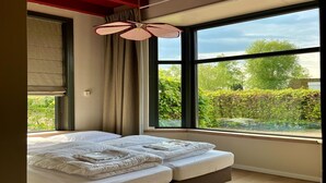 A modern bedroom with a large bed, a ceiling fan, and a view of greenery outside. - Luxury Group Retreat in Nature (Scherpenzeel)