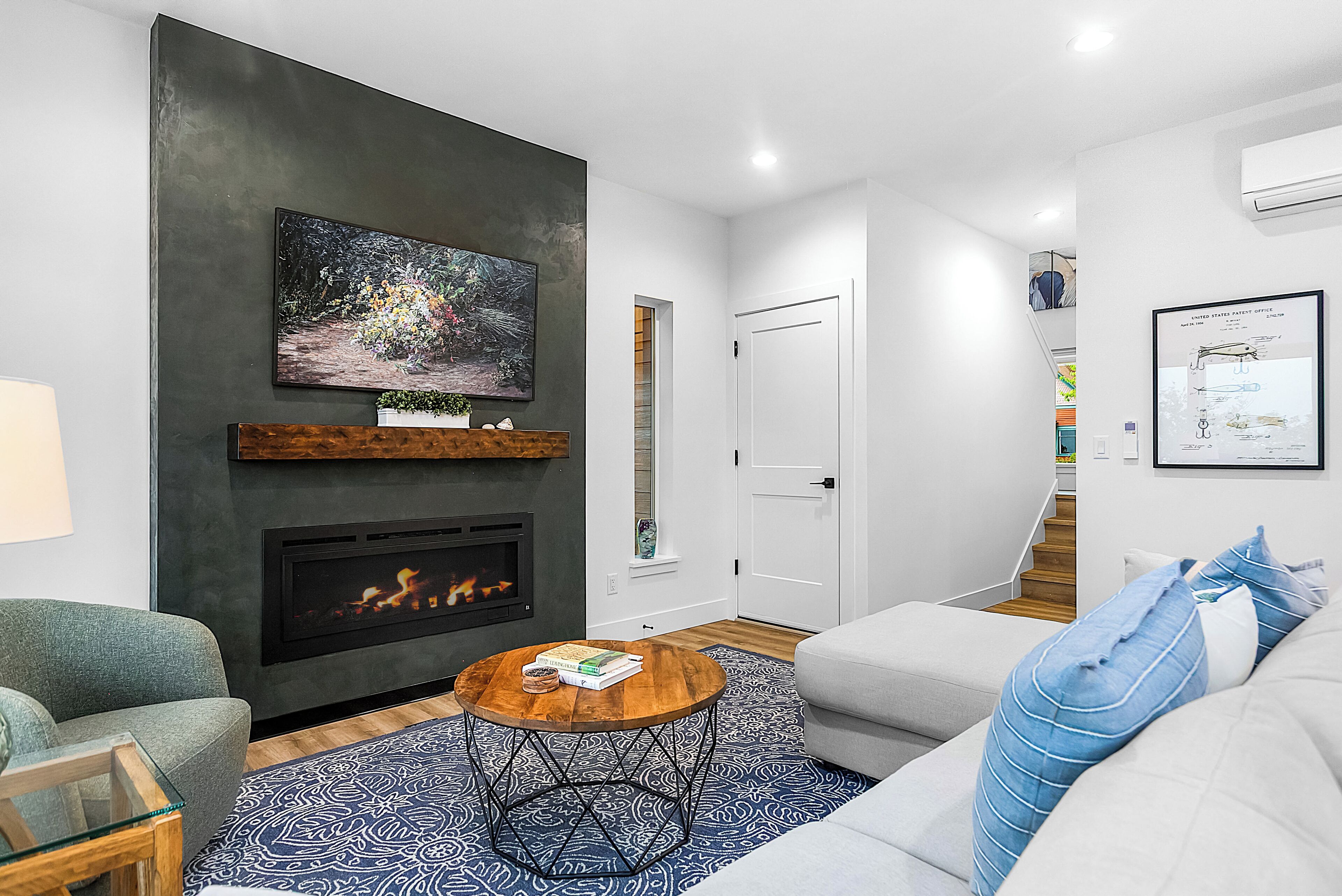 A modern living room with a fireplace, a round coffee table, a grey sofa, and a patterned rug.
