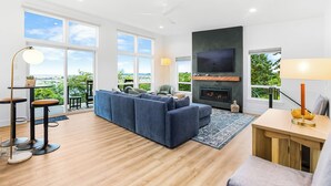 Una sala de estar moderna con un amplio sofá modular, un televisor de pantalla plana y una chimenea. Amplias ventanas ofrecen vistas al exterior.
