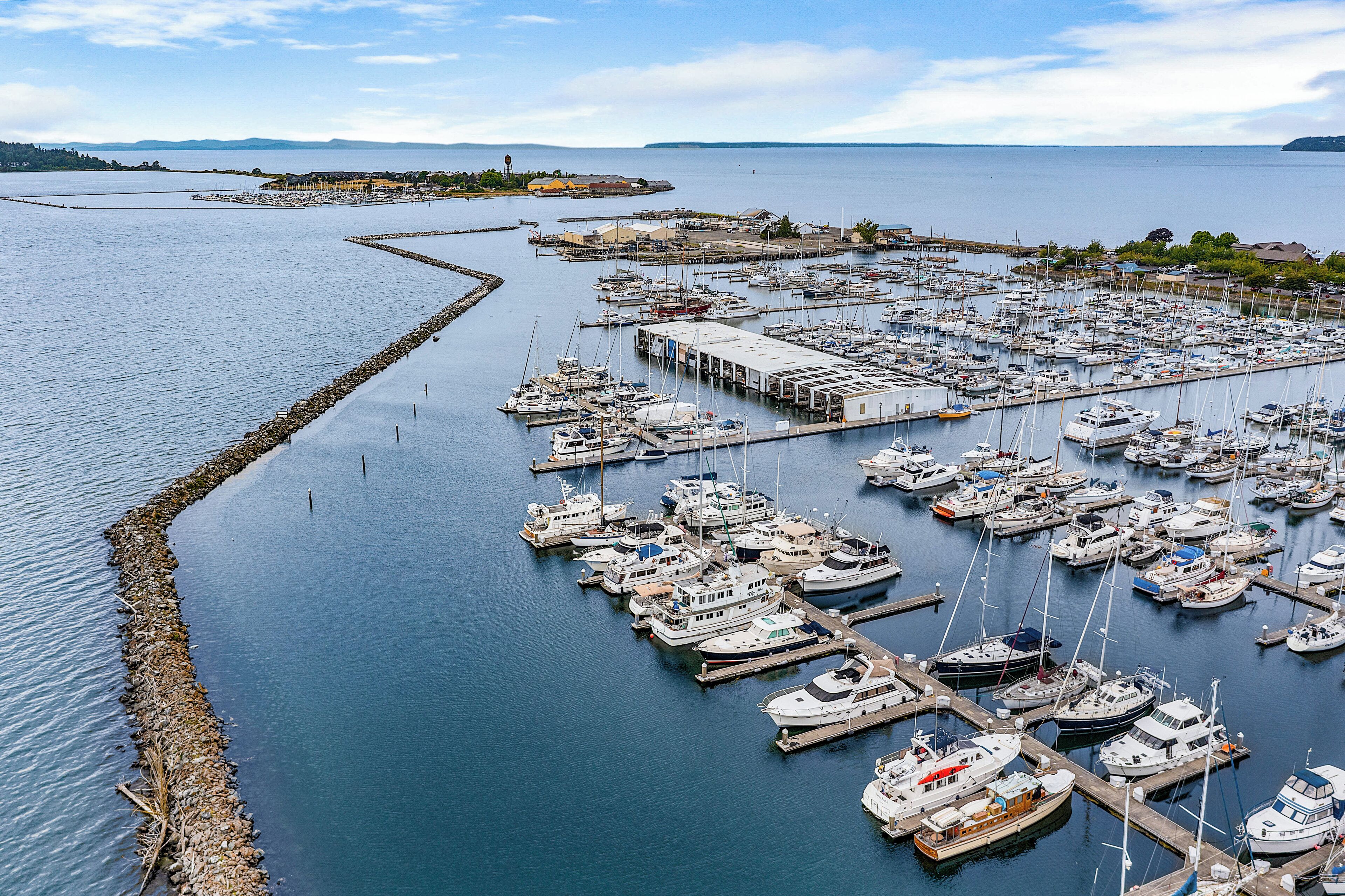 A marina with numerous boats docked at piers, surrounded by calm water and distant land.