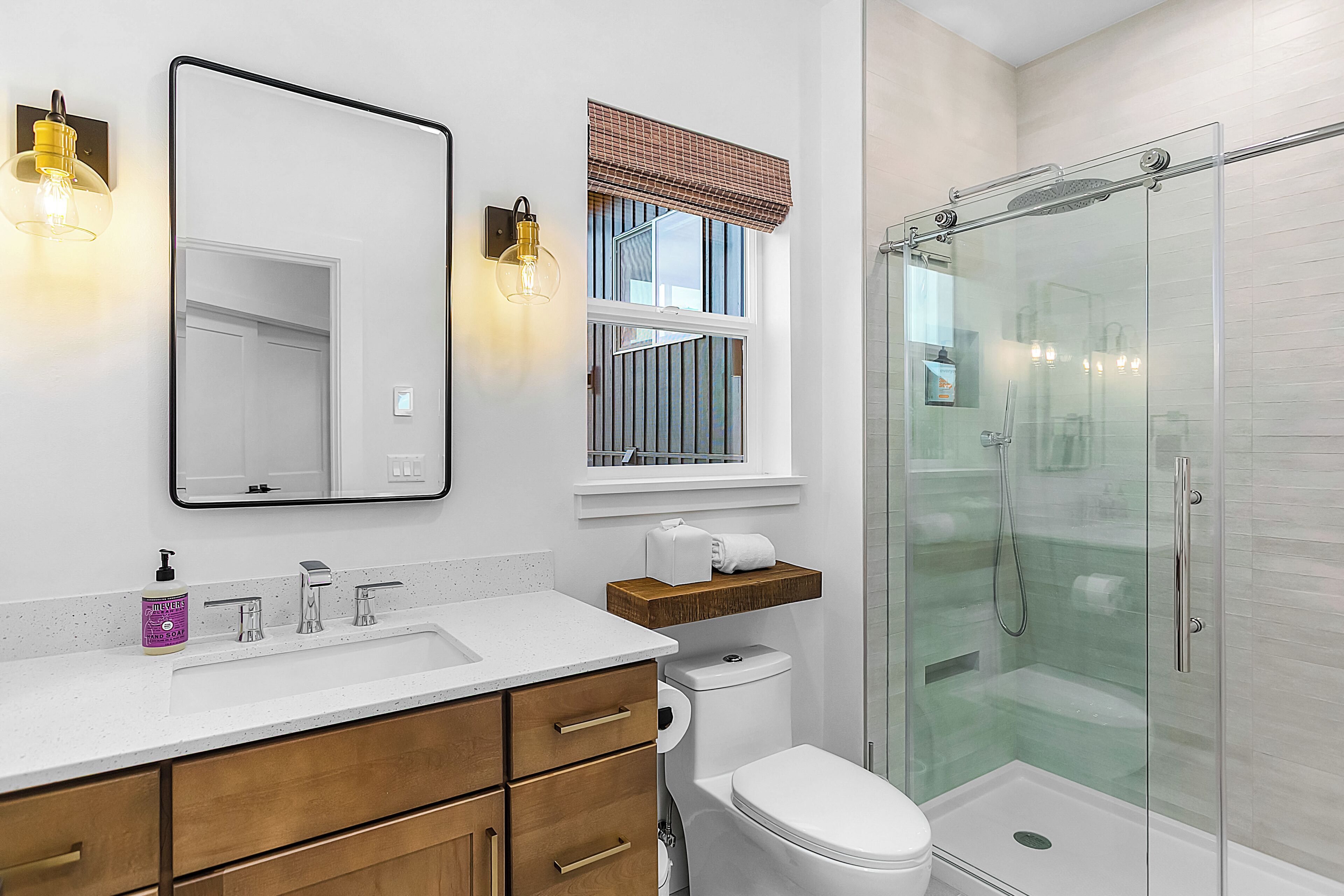 Een moderne badkamer met een grote spiegel, een toilet, een douche met glazen deuren en een houten plank boven de wastafel.