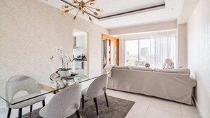 A modern living room with a glass dining table, two chairs, a beige sofa, and a city view through large windows. - Relaxing Ocean View Condo (Santo Domingo)