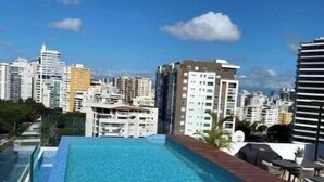 A rooftop swimming pool with clear blue water, surrounded by high-rise buildings and a clear sky. - Relaxing Ocean View Condo (Santo Domingo)