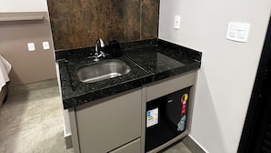 A compact kitchen with a granite countertop, stainless steel sink, and a built-in dishwasher. - Pousada Casa Limão (Rifaina)