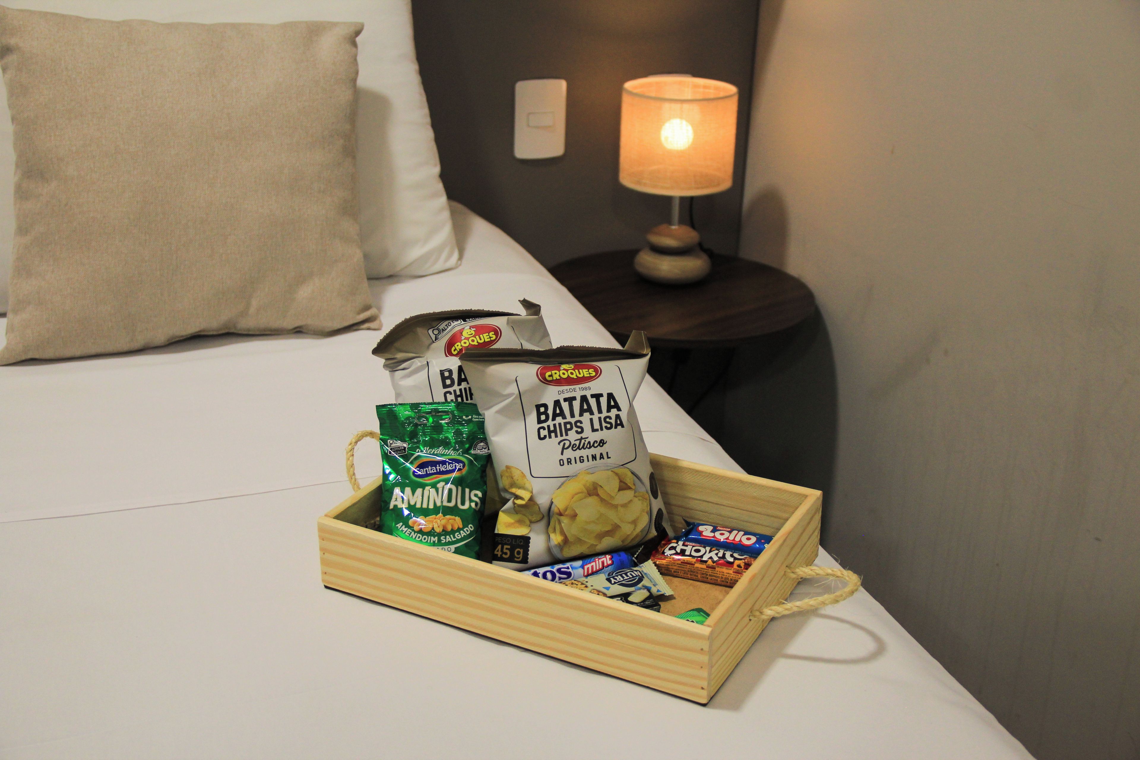 Una bandeja de madera con aperitivos y una bolsa de papas sobre una cama.
