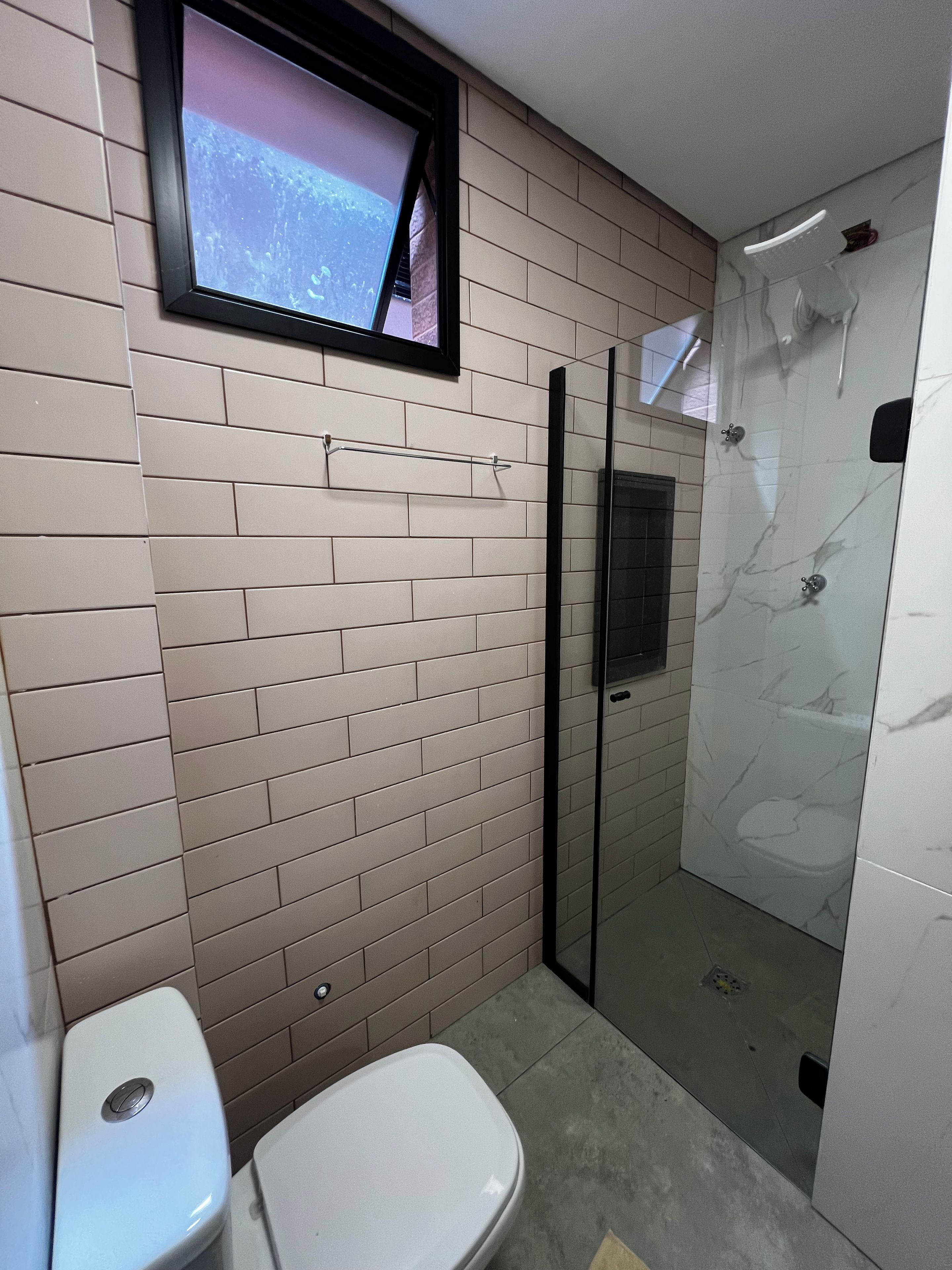 Casa de banho com sanita, chuveiro com porta de vidro e televisão na parede.