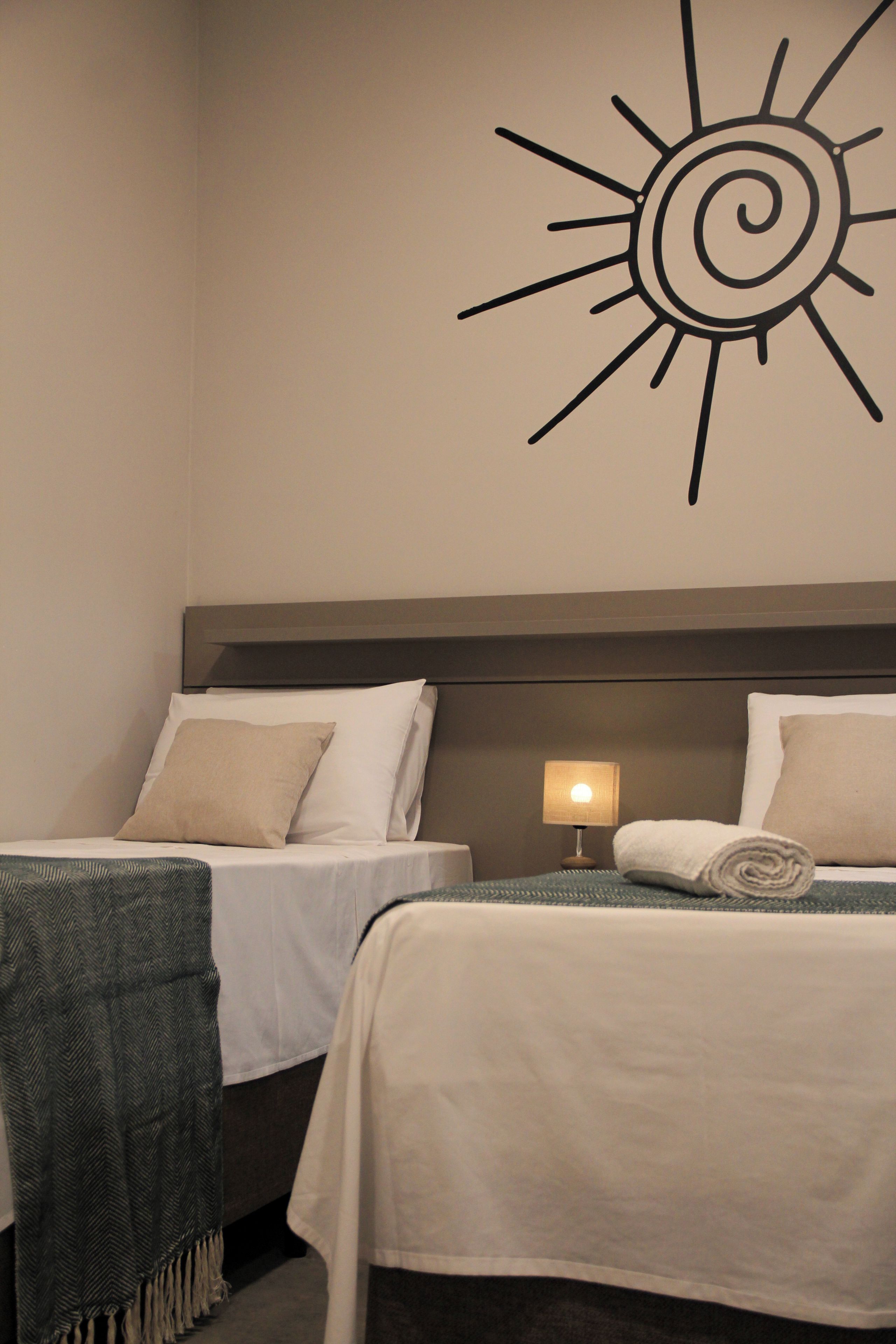Una habitació d'hotel amb dos llits, un adorn de sol penjat a la paret i una làmpada de nit.