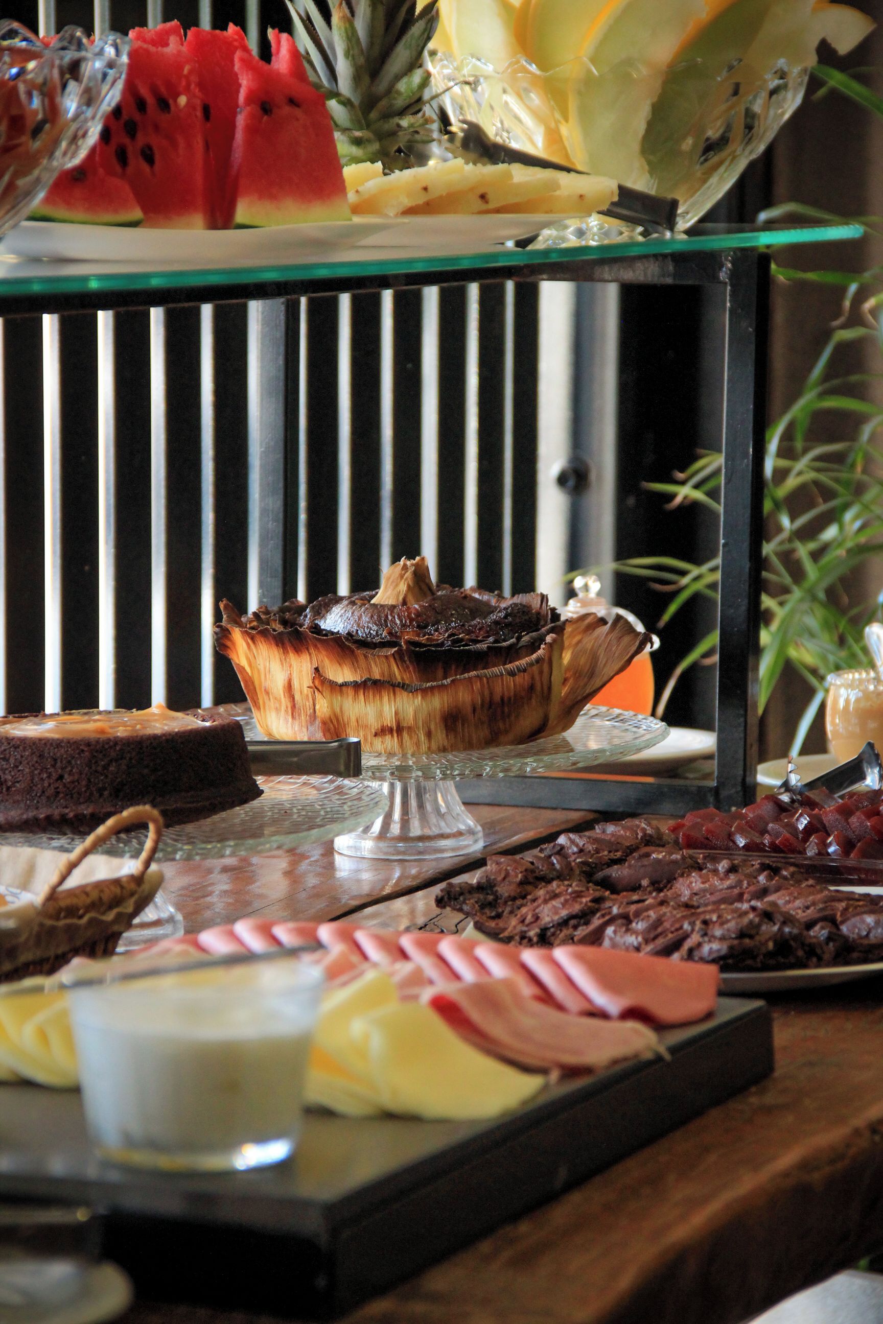 A buffet with various food items including a cake on a glass stand, fruits, and a selection of desserts.