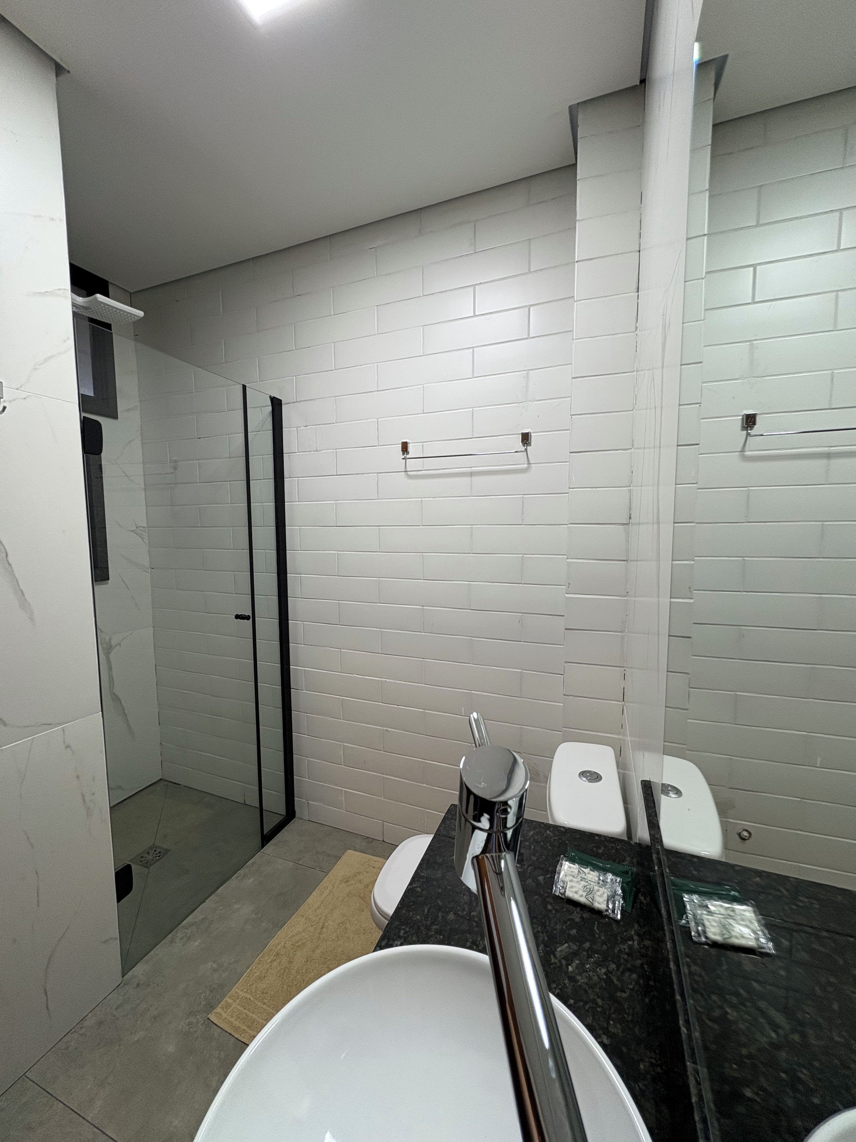 A bathroom with white subway tiles, a glass shower enclosure, a white sink with a black countertop, and a mirror above the sink.