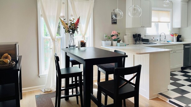 Une cuisine moderne avec des meubles blancs, un sol à carreaux noirs et blancs et un coin repas comprenant une table et des chaises noires.