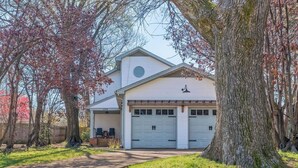 Une maison de plain-pied avec un garage, entourée d’arbres et d’une pelouse.