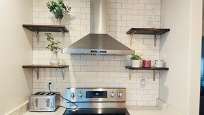 Une cuisine avec des carreaux de céramique blancs disposés en motif métro, des appareils électroménagers en acier inoxydable et des étagères en bois ornées de plantes.