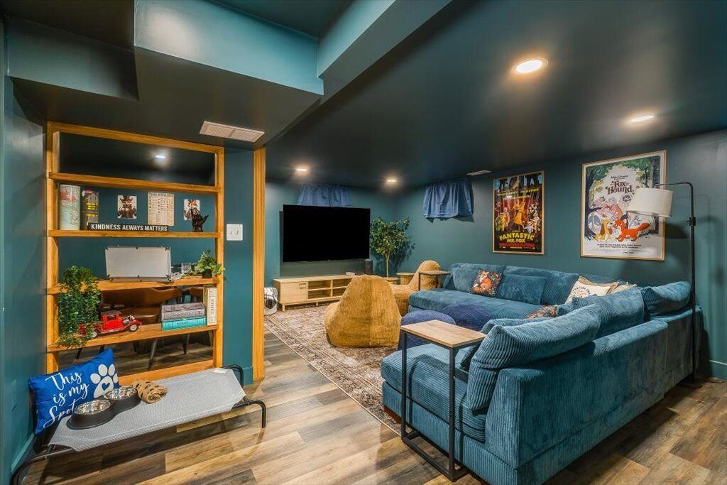 A cozy living room with a blue sofa, a wooden bookshelf, a flat-screen TV, and a pet bed.