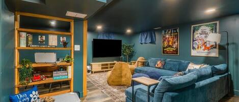 A cozy living room with a blue sofa, a wooden bookshelf, a flat-screen TV, and a pet bed.