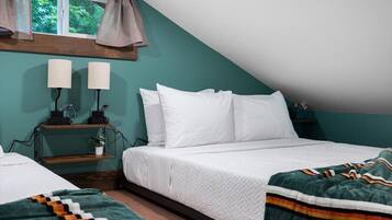A bedroom with a sloped ceiling, a bed with white bedding, a bedside table with lamps, and a window with curtains.