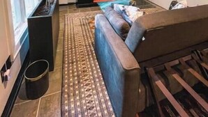 Uma sala de estar moderna com uma janela grande, um sofá, uma mesa de centro e uma tela de projetor exibindo uma paisagem natural.