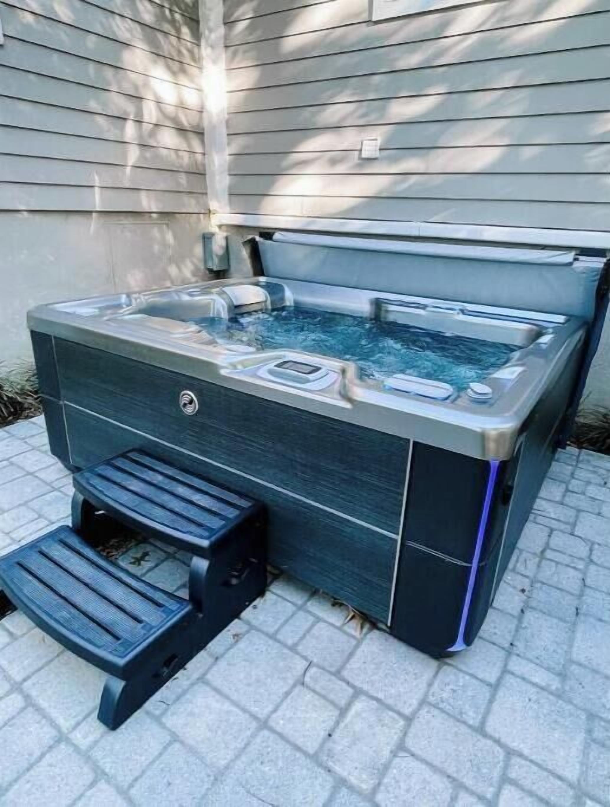 A hot tub with a built-in seat and steps, placed on a paved patio.