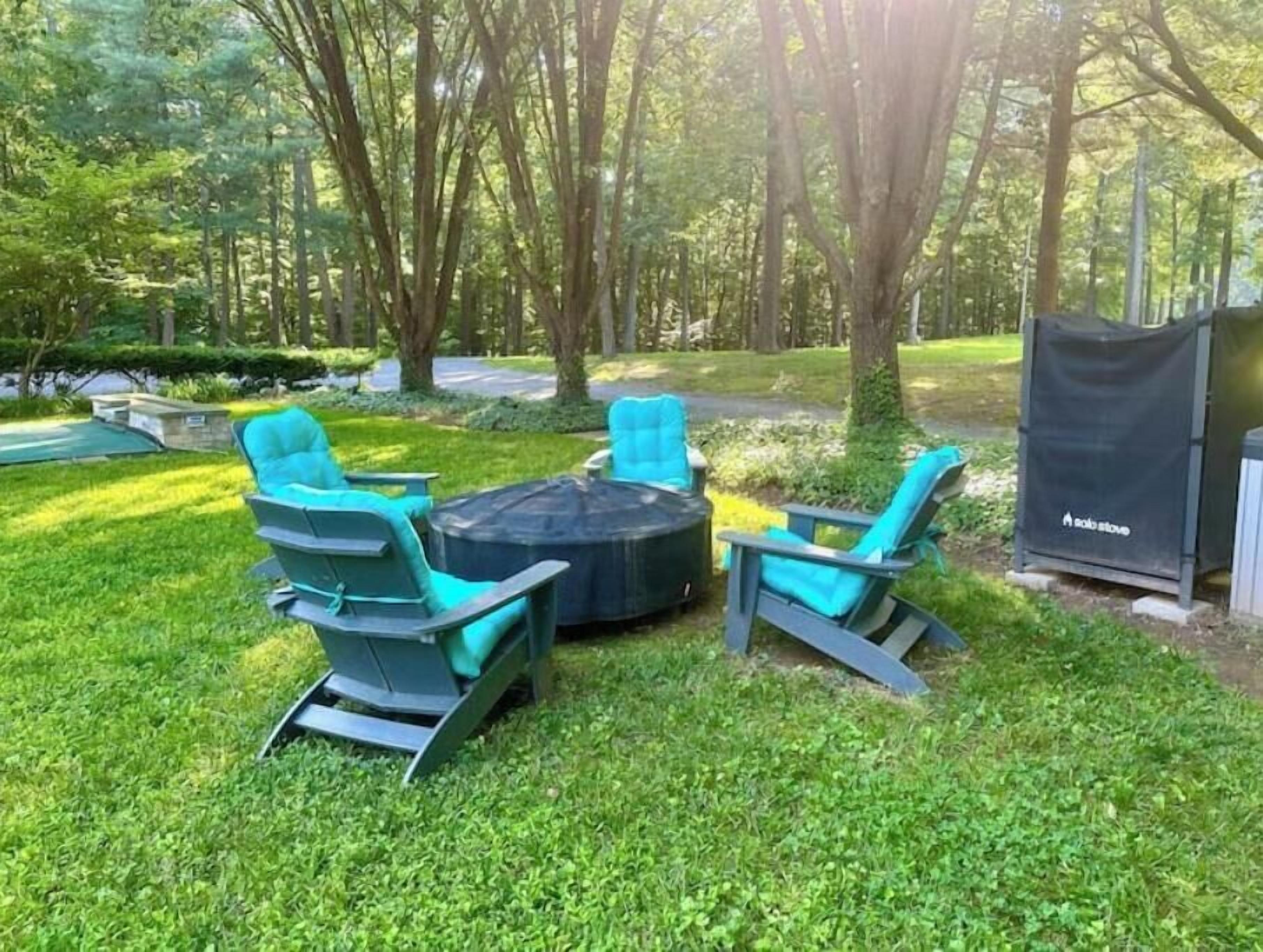 An outdoor seating area with a round table and four chairs, surrounded by a well-maintained lawn and trees.