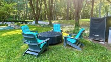 An outdoor seating area with a round table and four chairs, surrounded by a well-maintained lawn and trees.