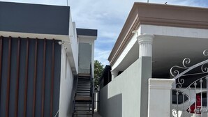 A residential property with a gated driveway, a staircase leading to a second floor, and a garage with a car parked inside.