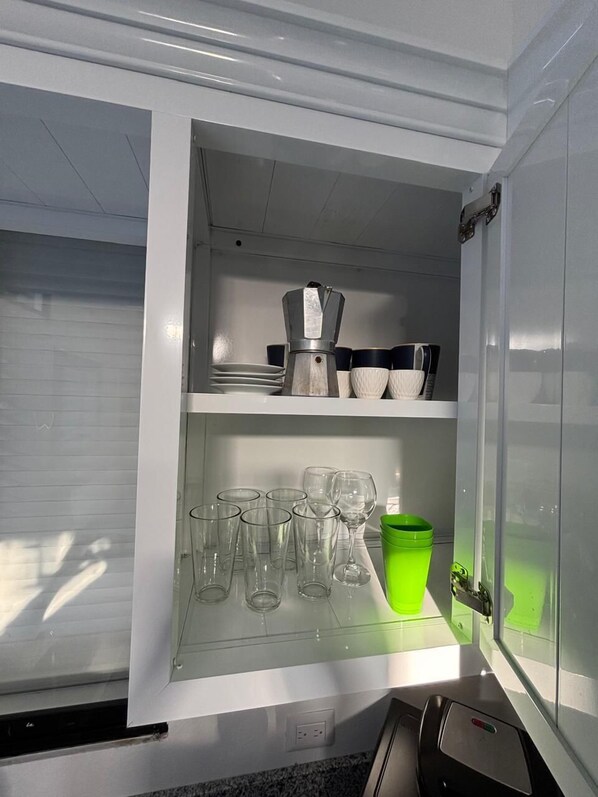 Una cocina con refrigerador empotrado, cafetera y diferentes vasos y vajilla.