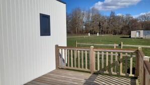 A wooden deck with a railing, a white building with a dark window, and a grassy field with trees in the background. - Calm and nature 40kms from Mt St Michel Chausey near Granville and beaches (Longueville)