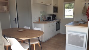 A compact kitchen with a stove, oven, microwave, and sink. There is a dining table with chairs and a window providing natural light. - Calm and nature 40kms from Mt St Michel Chausey near Granville and beaches (Longueville)