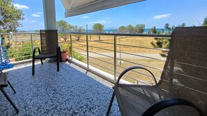 A balcony with two chairs, a potted plant, and a view of a road and greenery. - 100 meters from the blue flag awarded Mesi Beach. (Paralia Mesis)