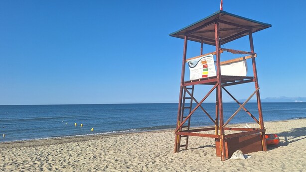 A wooden lifeguard tower with a sign on the side, located on a sandy beach with the ocean in the background. - 100 meters from the blue flag awarded Mesi Beach. (Paralia Mesis)