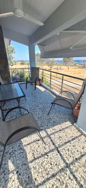 Un área de estar al aire libre techada con mesa y sillas, un ventilador de techo y vistas a un paisaje rural.