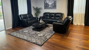 Sala de estar com sofá de couro preto, mesa de centro e tapete estampado.