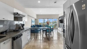 A modern kitchen with a built-in dishwasher, a stainless steel refrigerator, and a dining area with blue chairs. - 3rd-Floor Gem w/ Cruise Views & Rooftop Lounge (Puerto Vallarta)