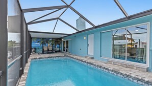 A swimming pool with a glass ceiling, a view of palm trees, and a door leading to an outdoor area.