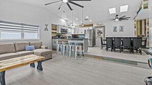 A modern open-plan living and dining area with a kitchen, a sofa, a dining table, and ceiling fans.